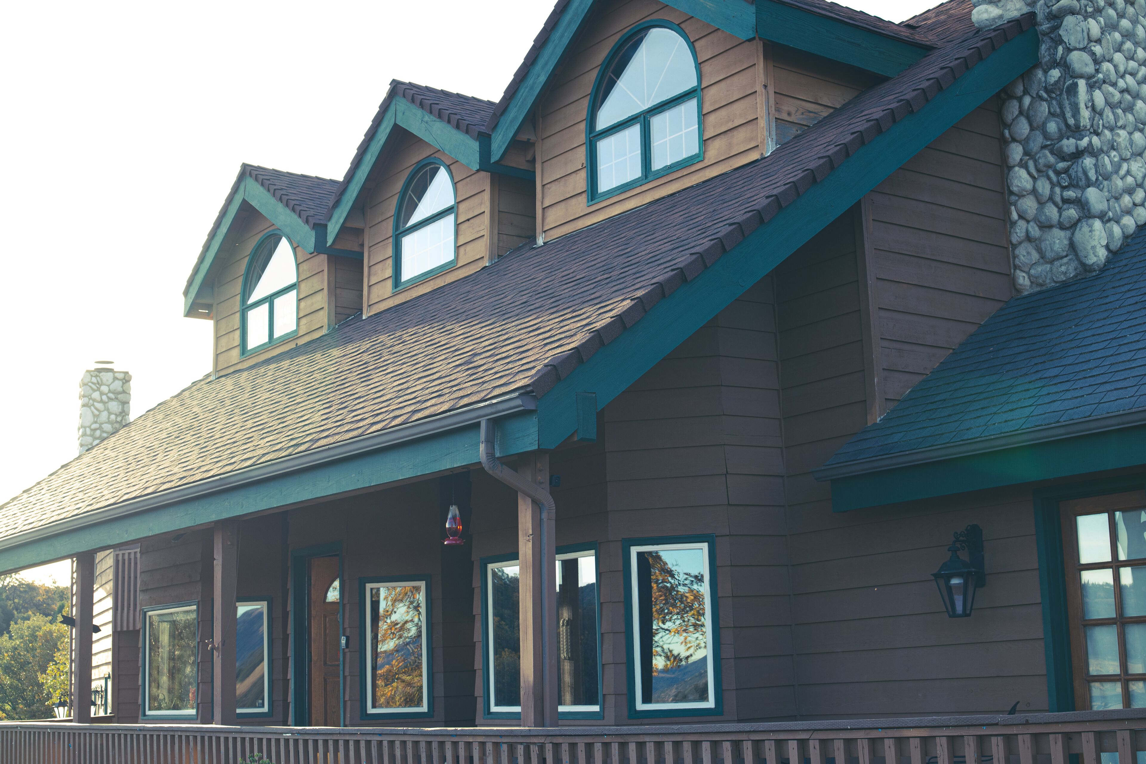 A two-story building with a stone chimney, wooden siding, and a covered porch with multiple windows.