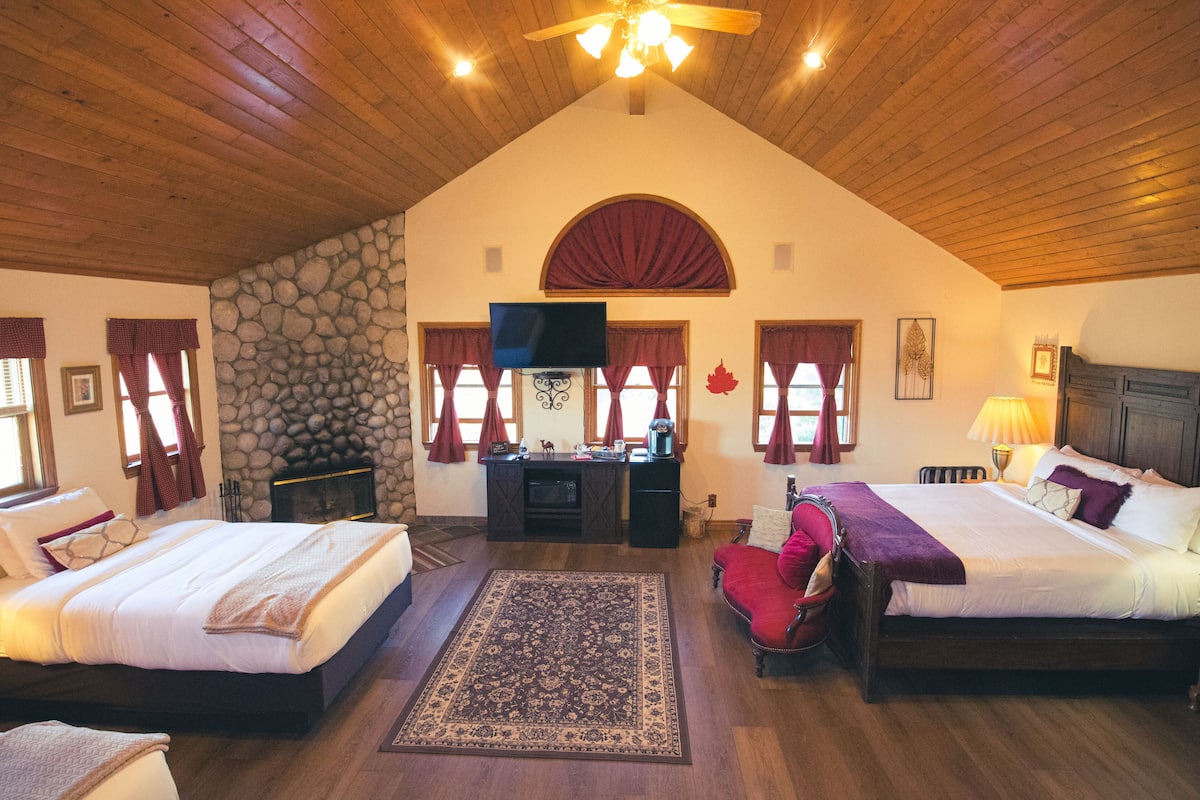A spacious room with two beds, a stone wall, a fireplace, and a television.