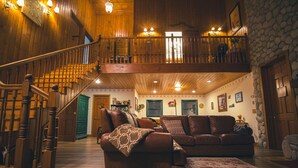 A spacious living area with a wooden staircase, a second-floor balcony, and a stone wall. - Tucker Peak Lodge (Julian)