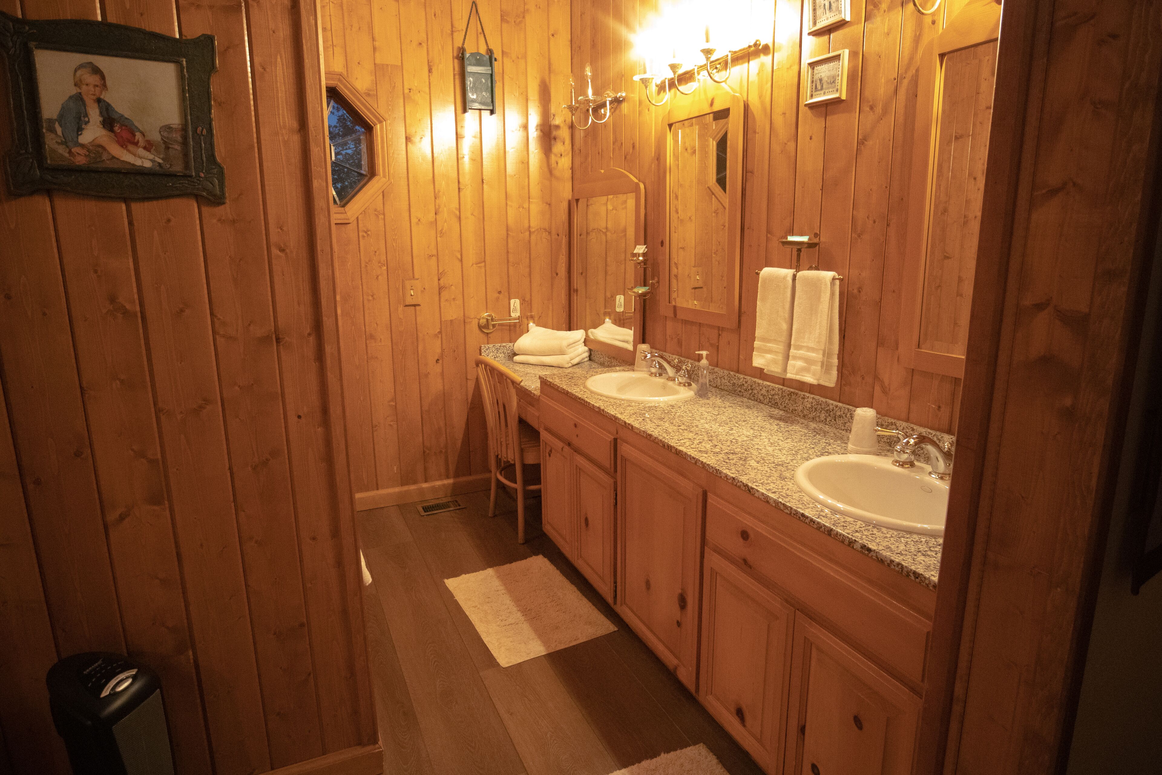 A wooden bathroom with two sinks, a mirror, and a framed picture on the wall.
