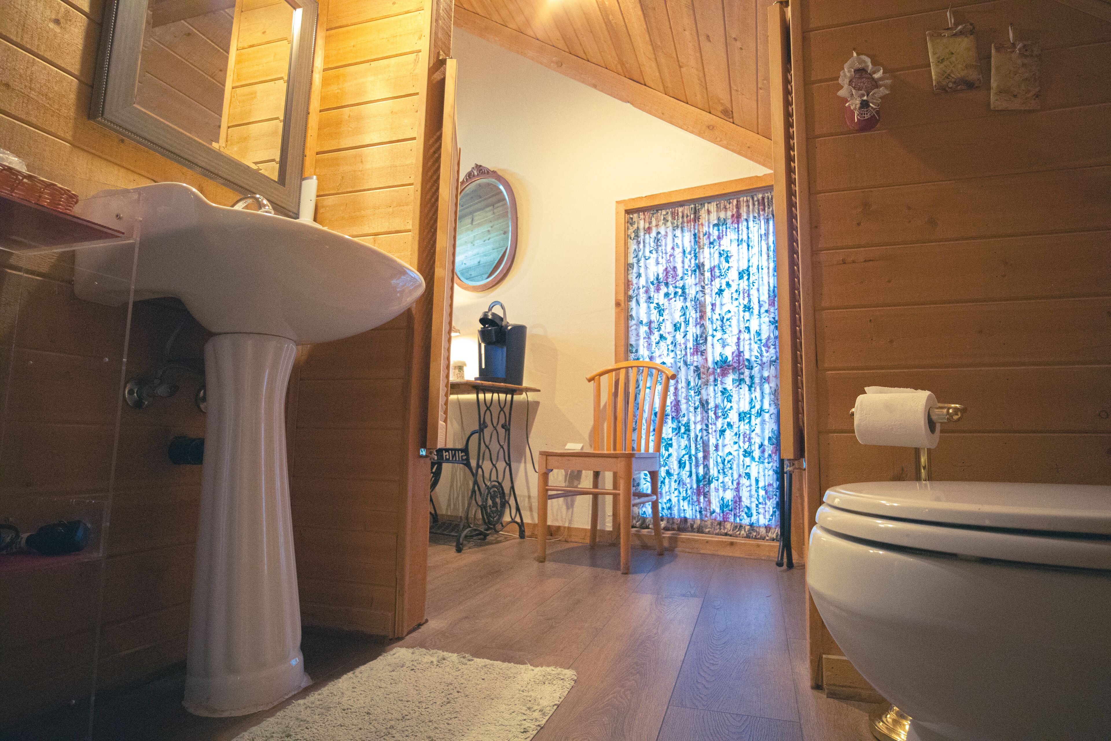 Un interno in legno con un lavabo bianco, una sedia di legno, un water e uno specchio.