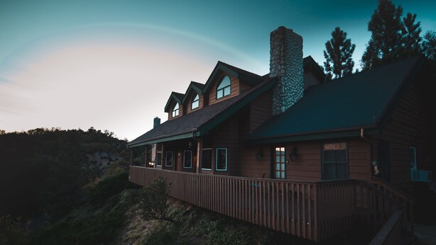 A large, two-story wooden house with a stone chimney, a covered porch, and a wooden deck. - Tucker Peak Lodge (Julian)