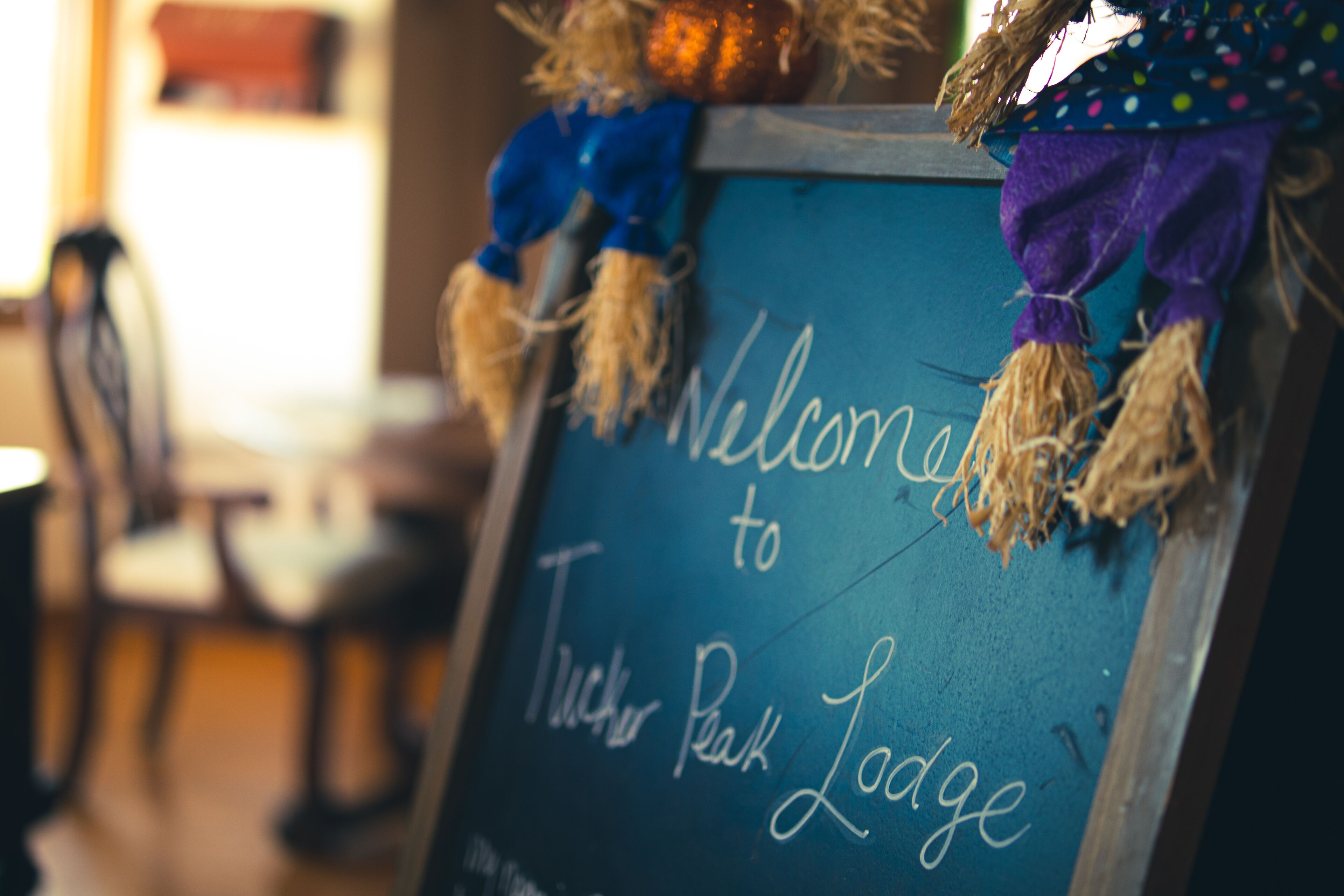 Een schoolbord met de tekst 'Welcome to Tucker Peak Lodge', een rustiek houten bord en een decoratieve figuur met een pompoen.