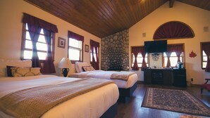 A hotel room with two beds, a stone wall, a fireplace, and a television. - Tucker Peak Lodge (Julian)