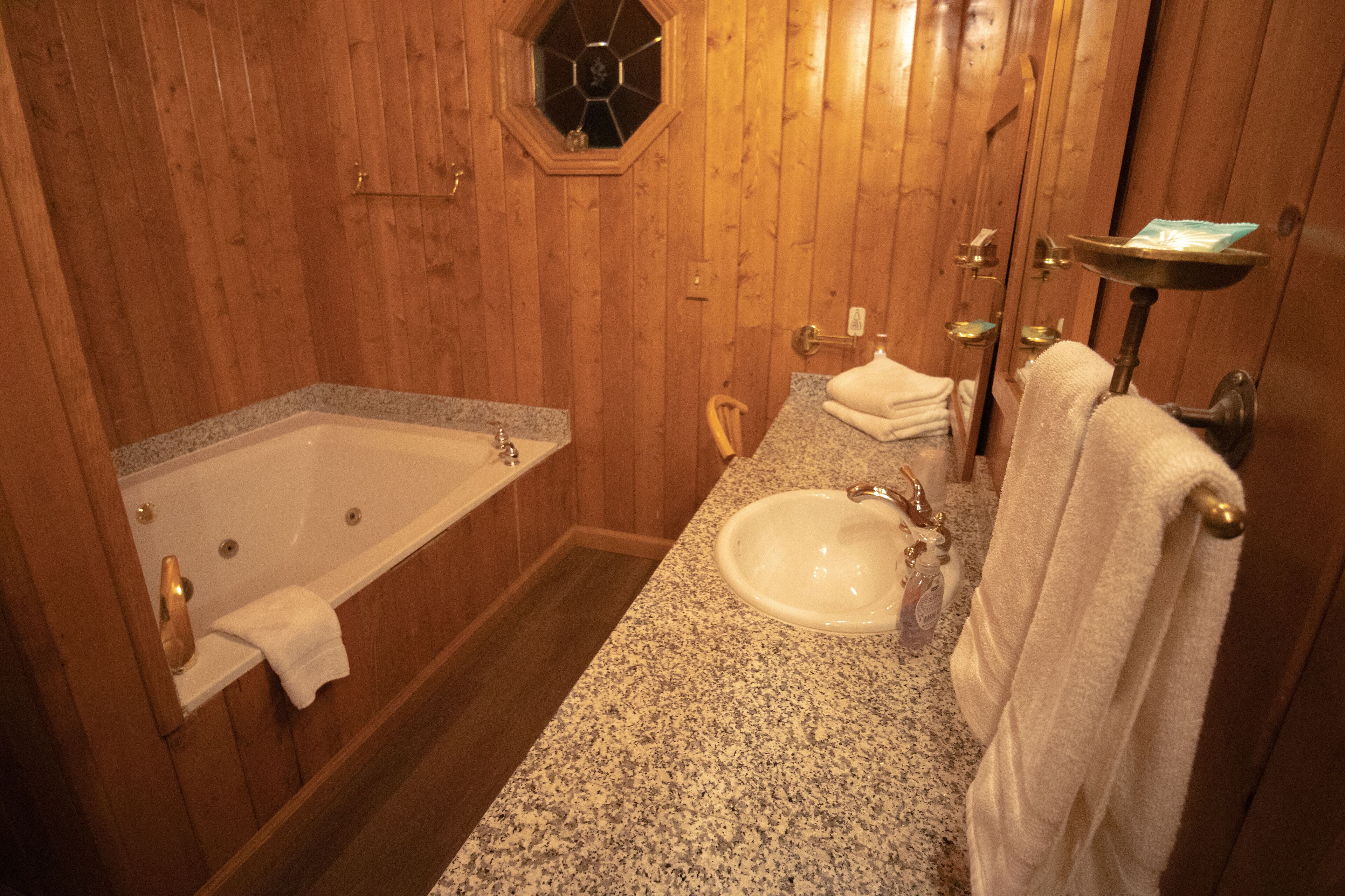 A wooden-paneled bathroom with a freestanding bathtub, a granite countertop sink, and a vanity mirror.
