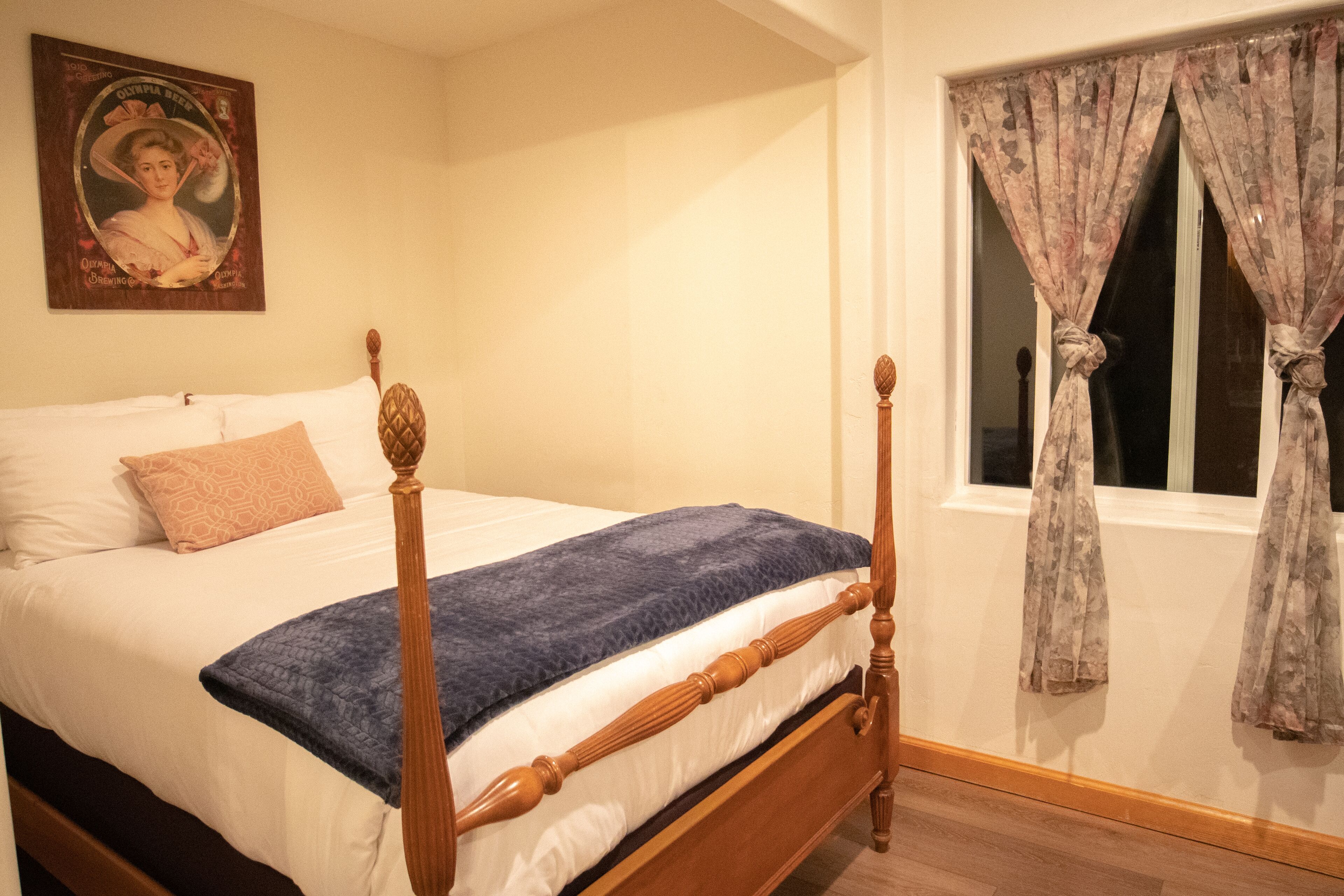 Un lit à baldaquin avec une couverture bleue, une tête de lit en bois et un rideau à motifs floraux à une fenêtre.