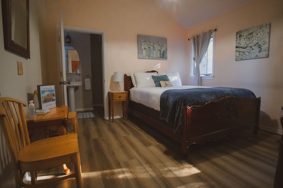 A bedroom with a wooden bed, a bedside table, a chair, and a desk.