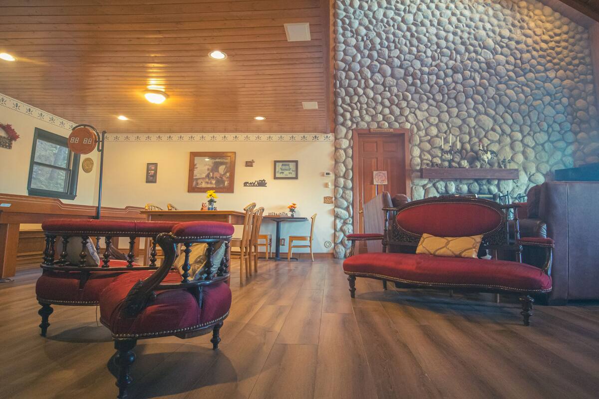 A room with a wooden ceiling, stone wall, and a fireplace. There are two red upholstered chairs and a wooden table with chairs.