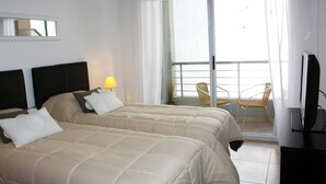A hotel room with two beds, a balcony with chairs, a TV, and a window with curtains. - Arenales Suites (Buenos Aires)
