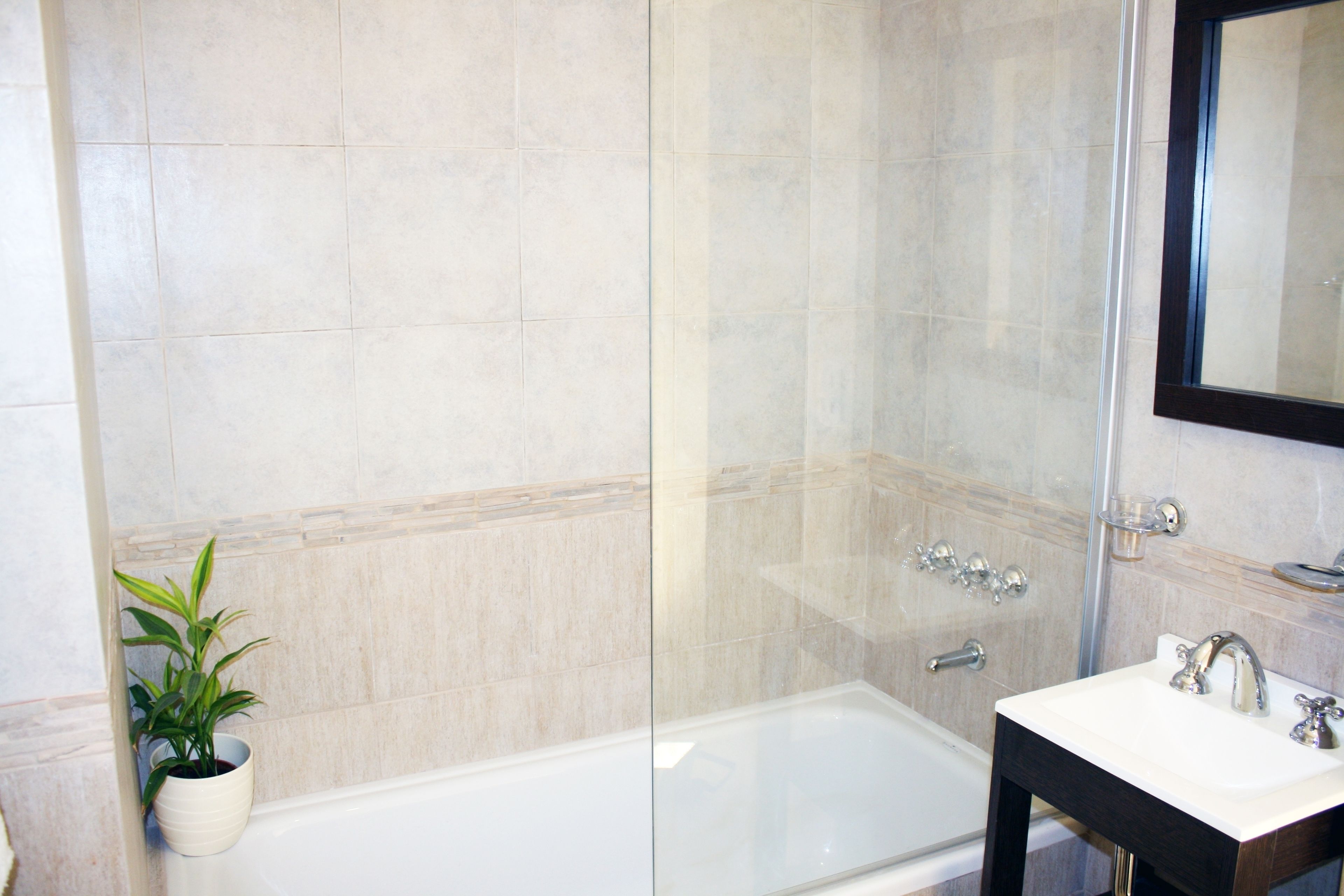 A modern bathroom with a glass-enclosed shower, a white bathtub, and a sink with a mirror above it.