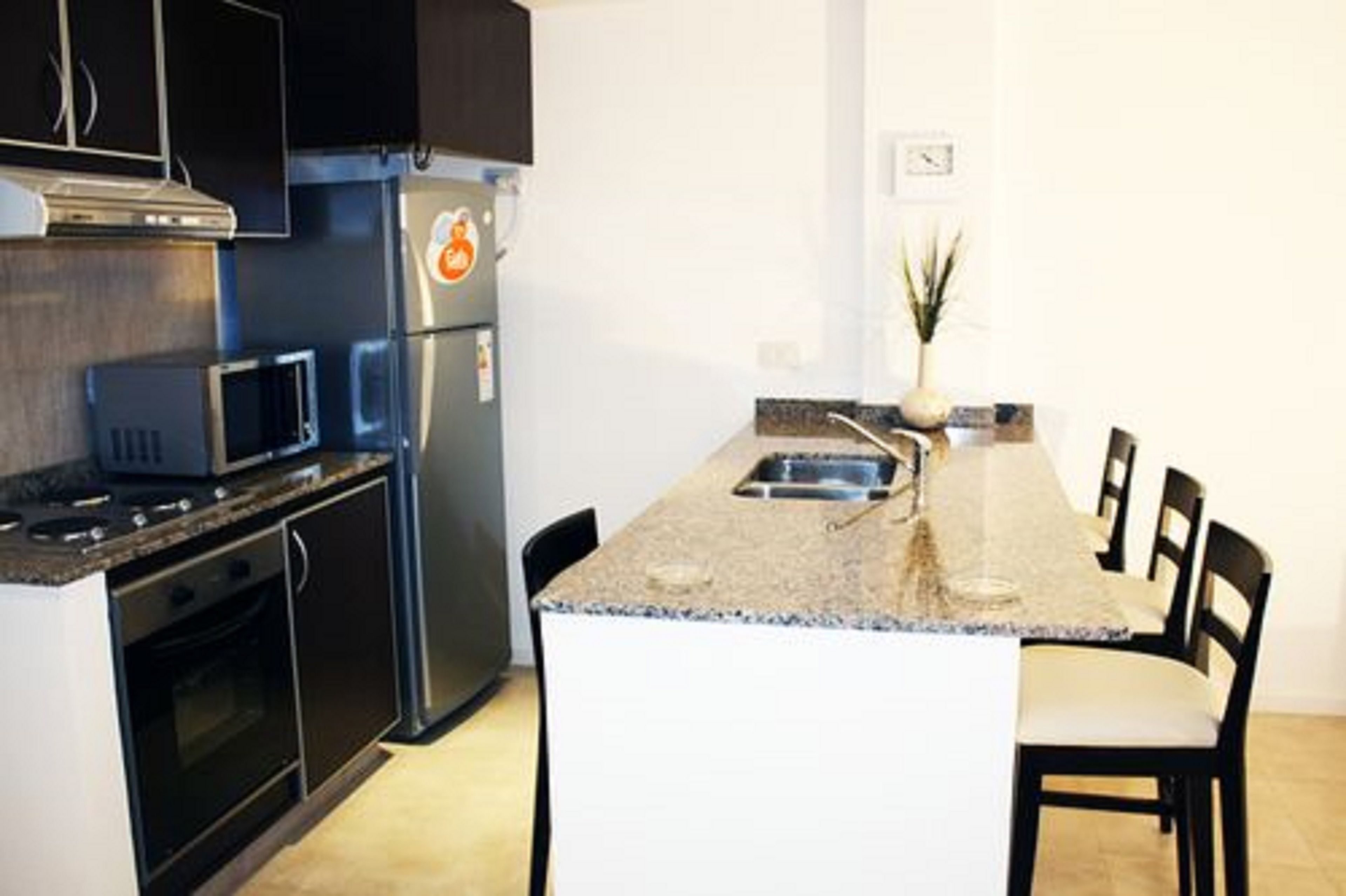 A compact kitchen with a microwave, stove, oven, and refrigerator. There is a small dining area with a sink and chairs.