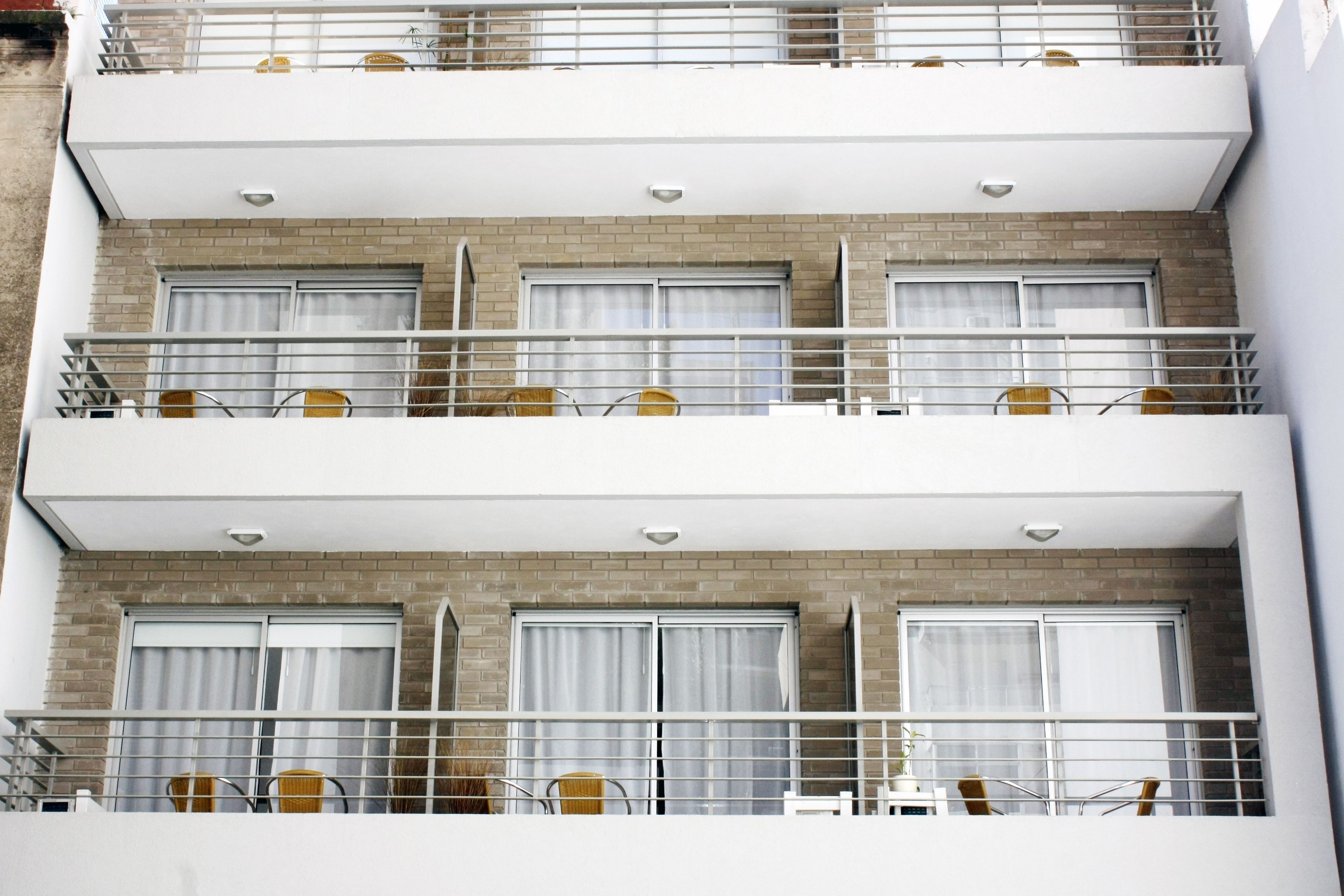Un hotel de varios pisos con balcones en cada planta, con barandas blancas y sillas de mimbre.