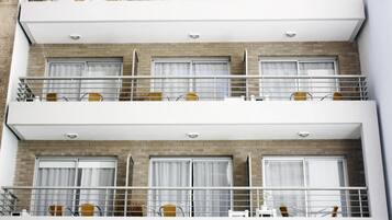Un hotel de varios pisos con balcones en cada planta, con barandas blancas y sillas de mimbre.