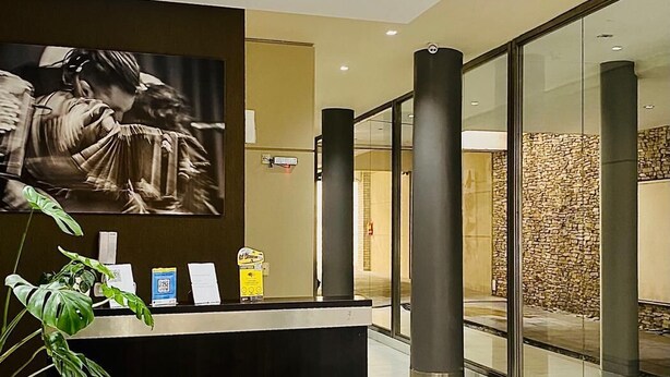 A modern reception area with a reception desk, a large wall-mounted artwork, and a stone wall in the background. - Arenales Suites (Buenos Aires)