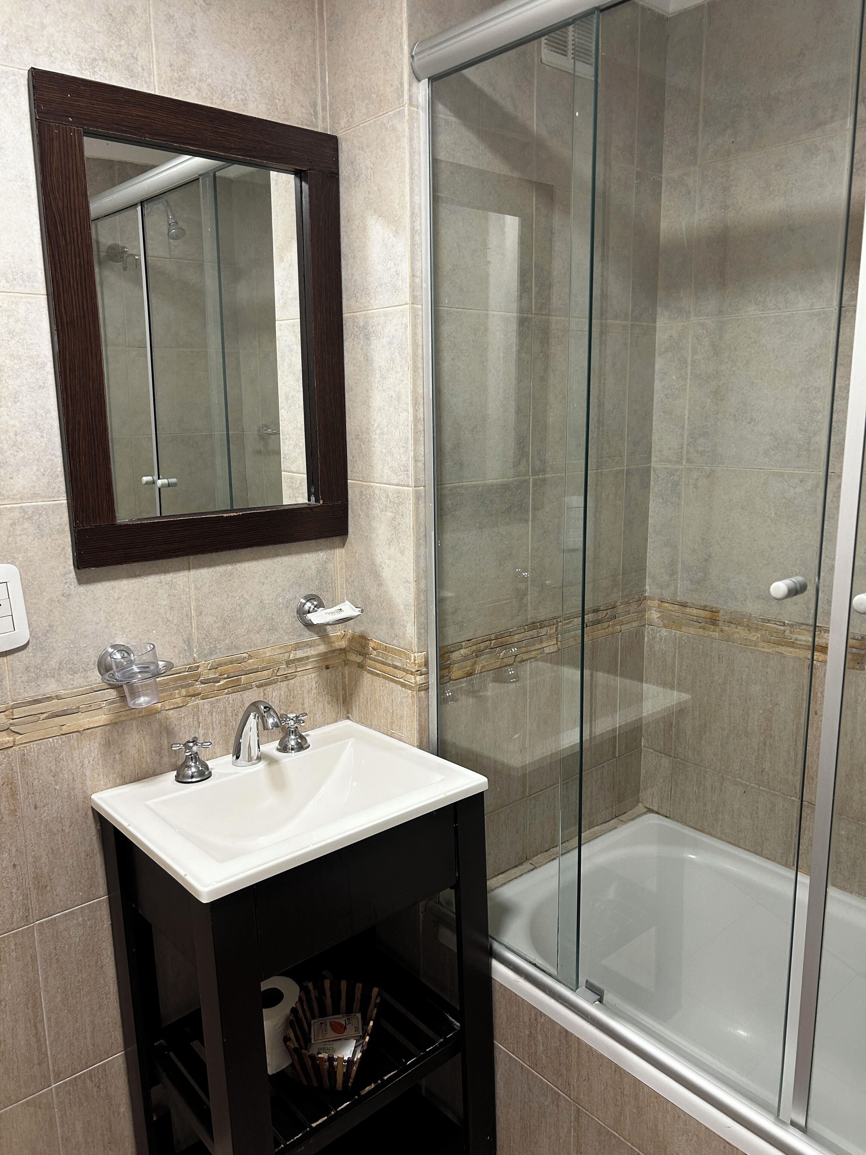 A bathroom with a glass shower enclosure, a white sink, and a mirror with a wooden frame.
