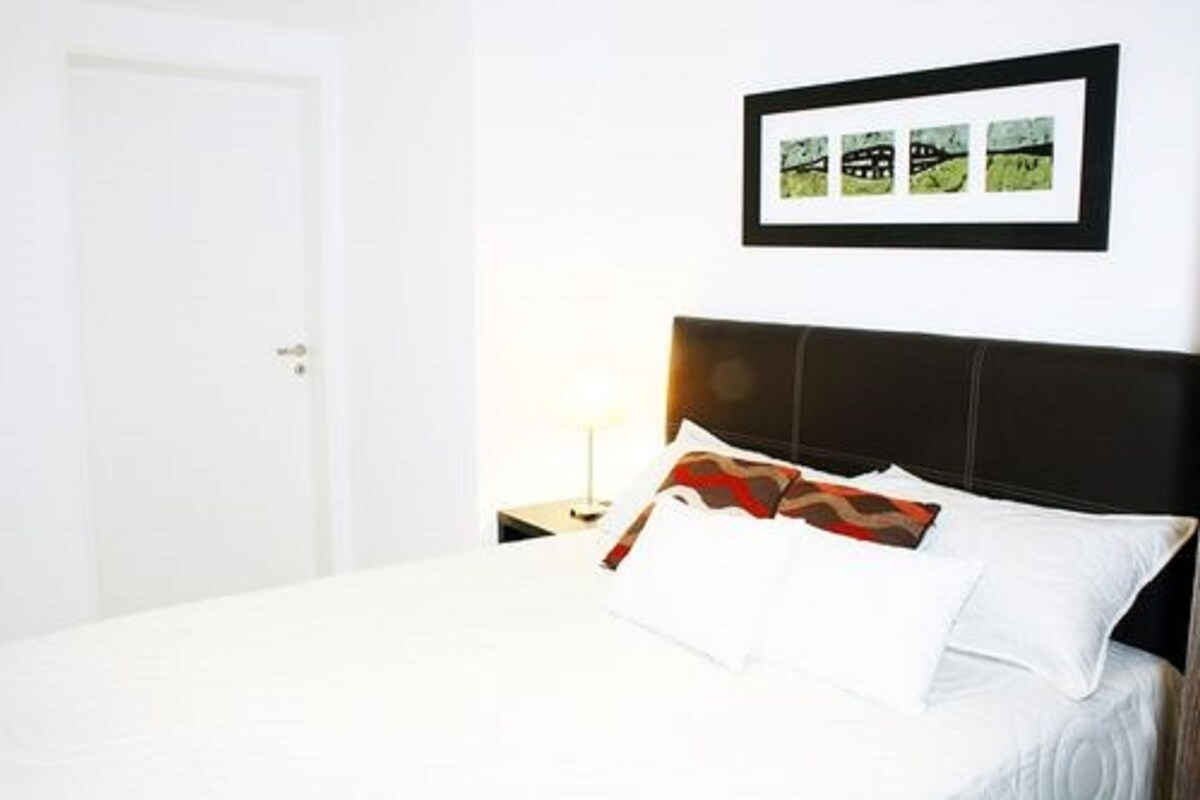 A neatly made bed with white bedding, a dark headboard, and a framed picture above it.