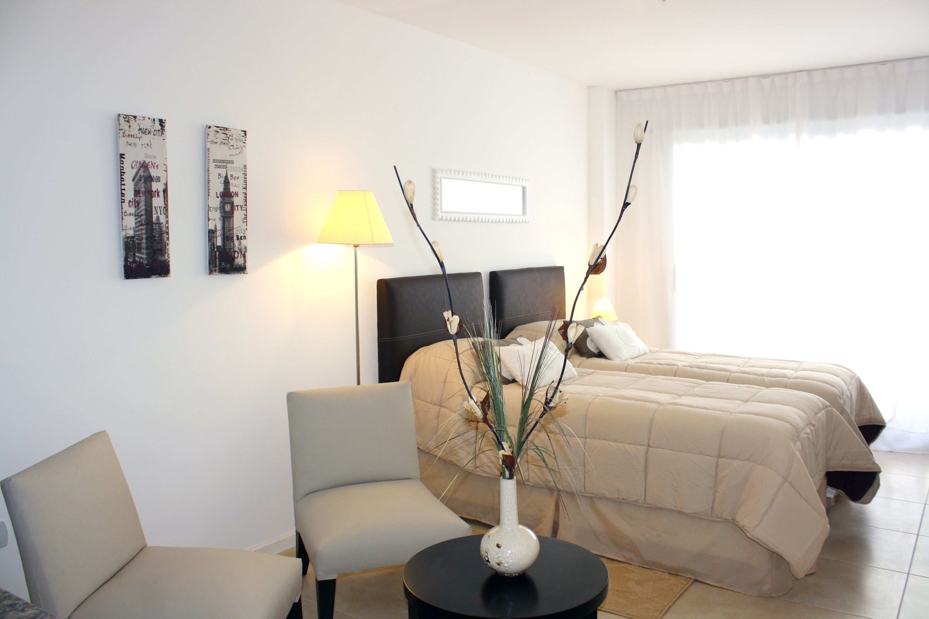 Ein Hotelzimmer mit einem Bett, einem Sessel, einem kleinen Tisch mit einer Vase und zwei Wandbildern.