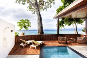 A wooden deck with a pool, lounge chairs, and a view of the ocean.