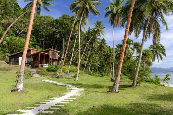 A wooden house with a porch, surrounded by palm trees and a pathway leading to the beach. - The Remote Resort, Fiji Islands (Nawi)