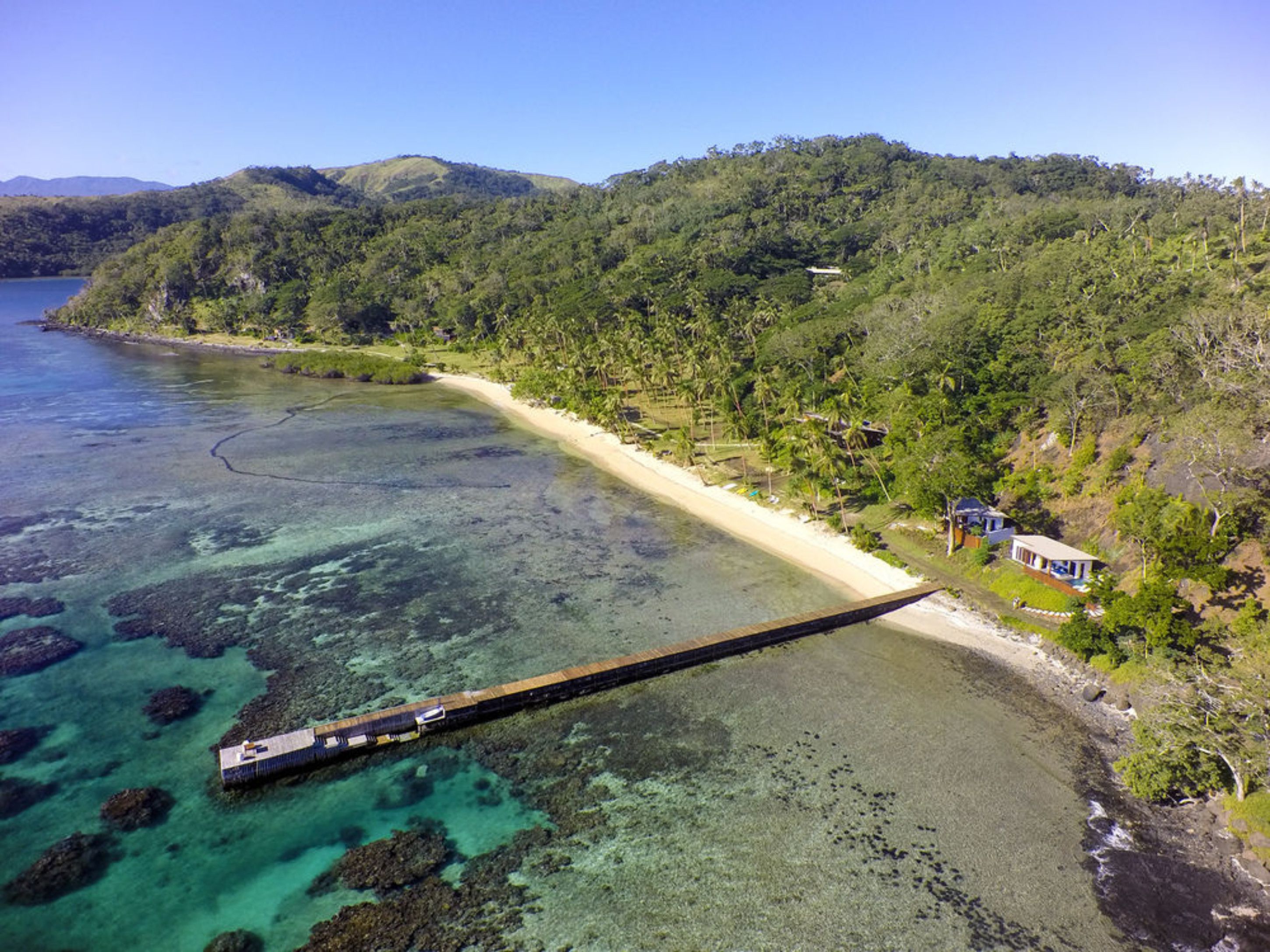 A coastal area with a pier extending into turquoise waters, surrounded by lush greenery and a small building on the shore.