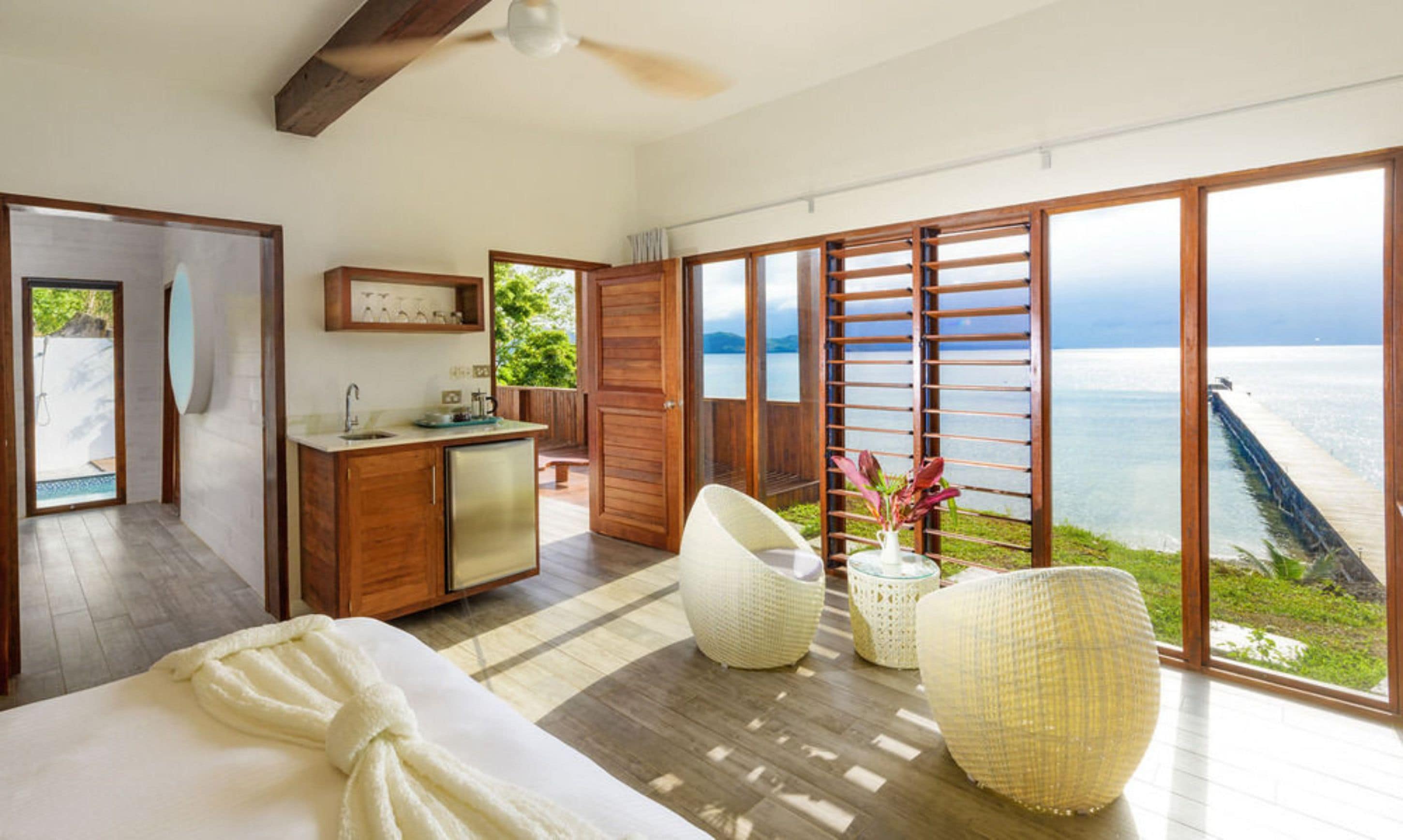 A bedroom with a large bed, a wooden desk, a bathroom, and a view of the sea.