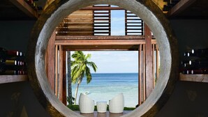 A circular window with a view of a palm tree and the ocean. - The Remote Resort, Fiji Islands (Nawi)
