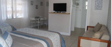 Een hotelkamer met twee bedden, een televisie, een bureau met stoelen en een zichtbare badkamer door een geopende deur.
