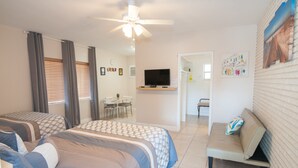 Habitación de hotel con dos camas, televisor, ventilador de techo, sofá y zona de comedor.