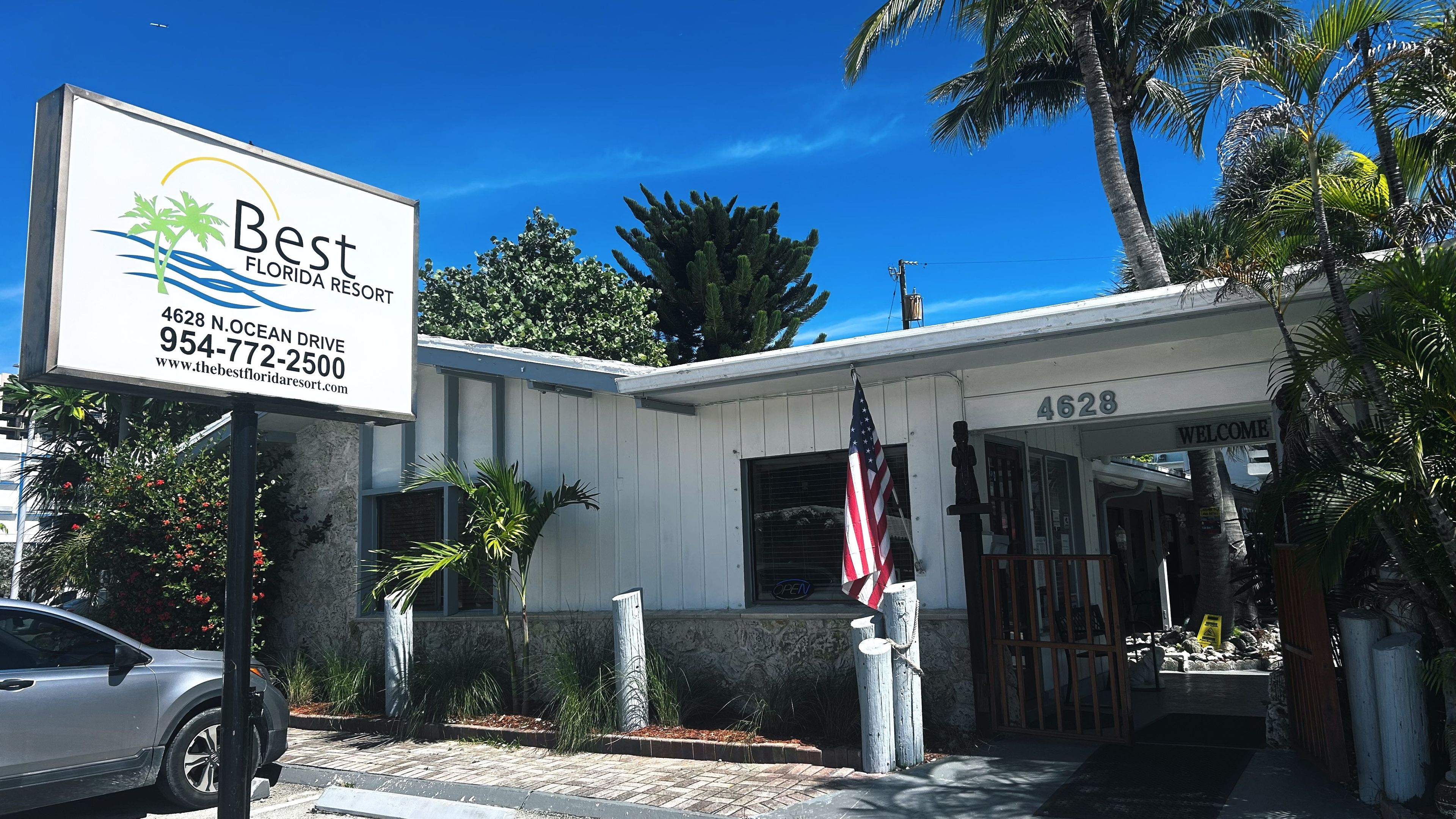 A Best Florida Resort building with a clear sky, palm trees, and a signboard.