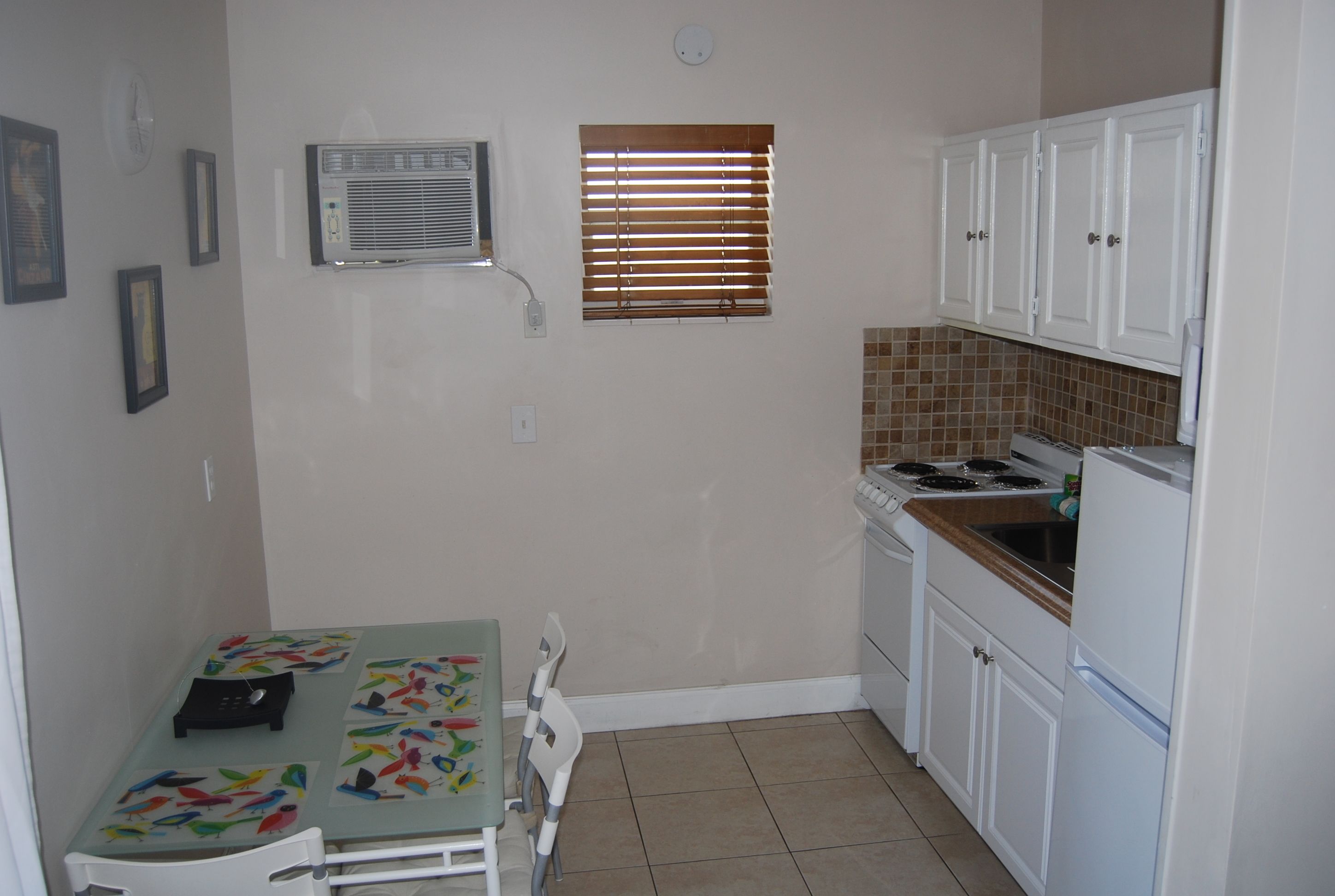 A compact kitchen with white cabinets, a stove, and a small dining table with chairs.