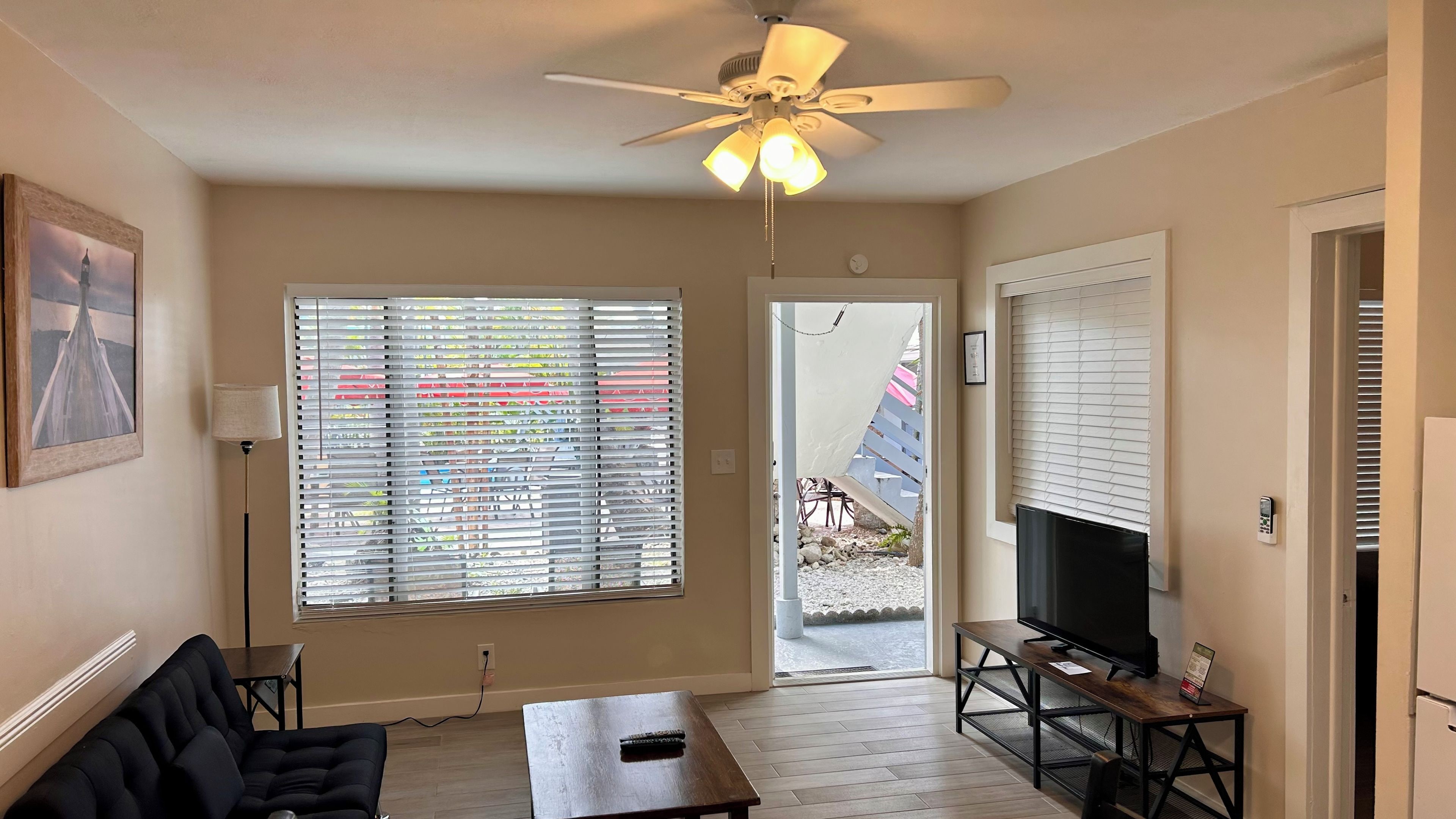 Un salon avec un ventilateur de plafond, un téléviseur posé sur un meuble en bois, un canapé et une table.