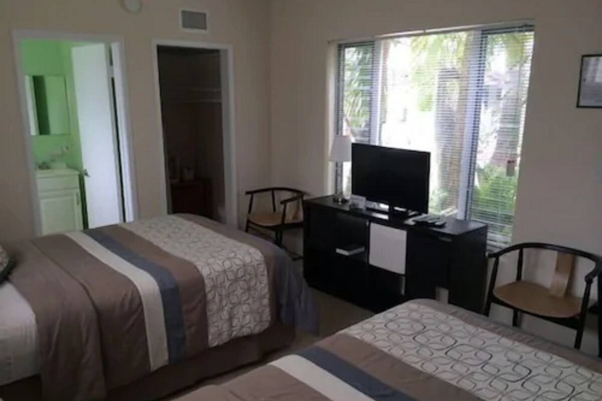 A hotel room with two beds, a desk with a television, and a window with blinds.