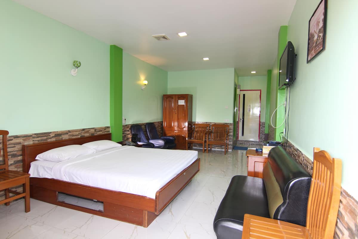 A hotel room with a large bed, a wooden bench, a television, and a small table.