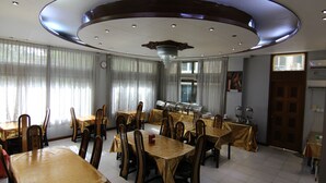 A dining area with multiple tables and chairs, a ceiling with circular lighting, and a clock on the wall.