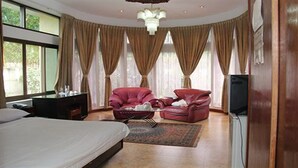 A hotel room with a bed, a desk, a red leather chair, a television, and large windows with curtains.