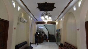 A hotel reception area with a chandelier, reception desk, and a staircase leading to another floor.