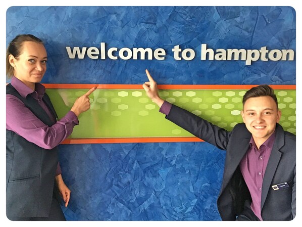 Une pancarte d’accueil avec l’inscription « Bienvenue à Hampton » et deux personnes la pointant du doigt.