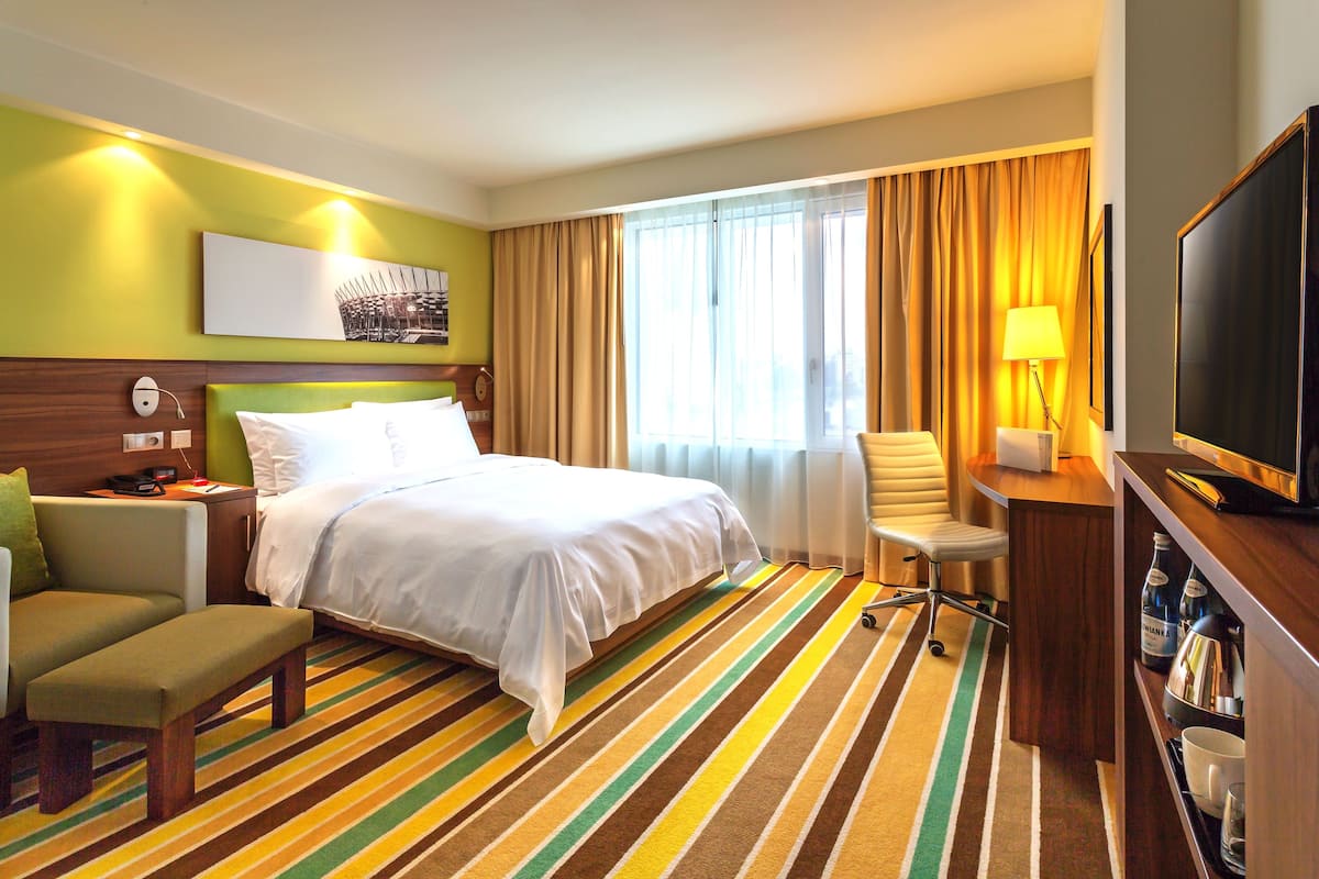 Une chambre d’hôtel équipée d’un lit, d’un bureau, d’une chaise, d’une télévision et d’une fenêtre avec des rideaux.