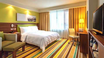 A hotel room with a bed, a desk, a chair, a TV, and a window with curtains.