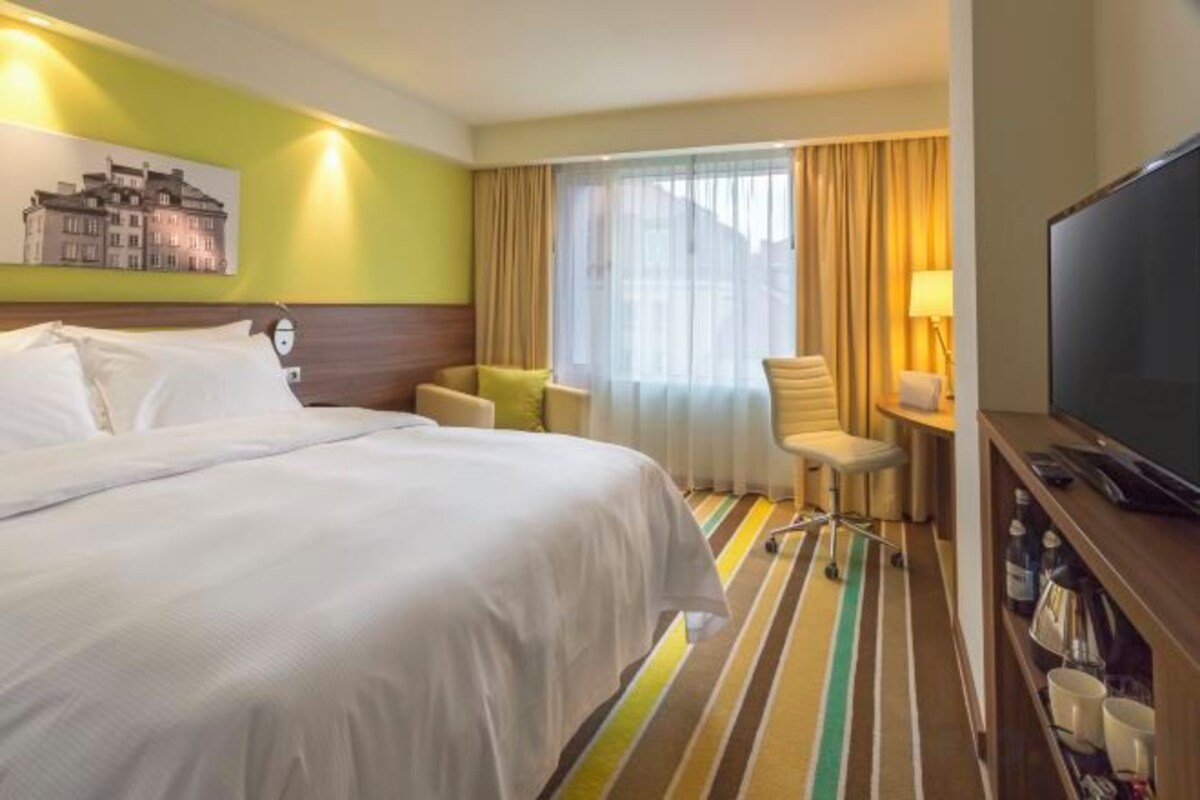 A hotel room with a bed, a television, a desk with a lamp, and a chair.