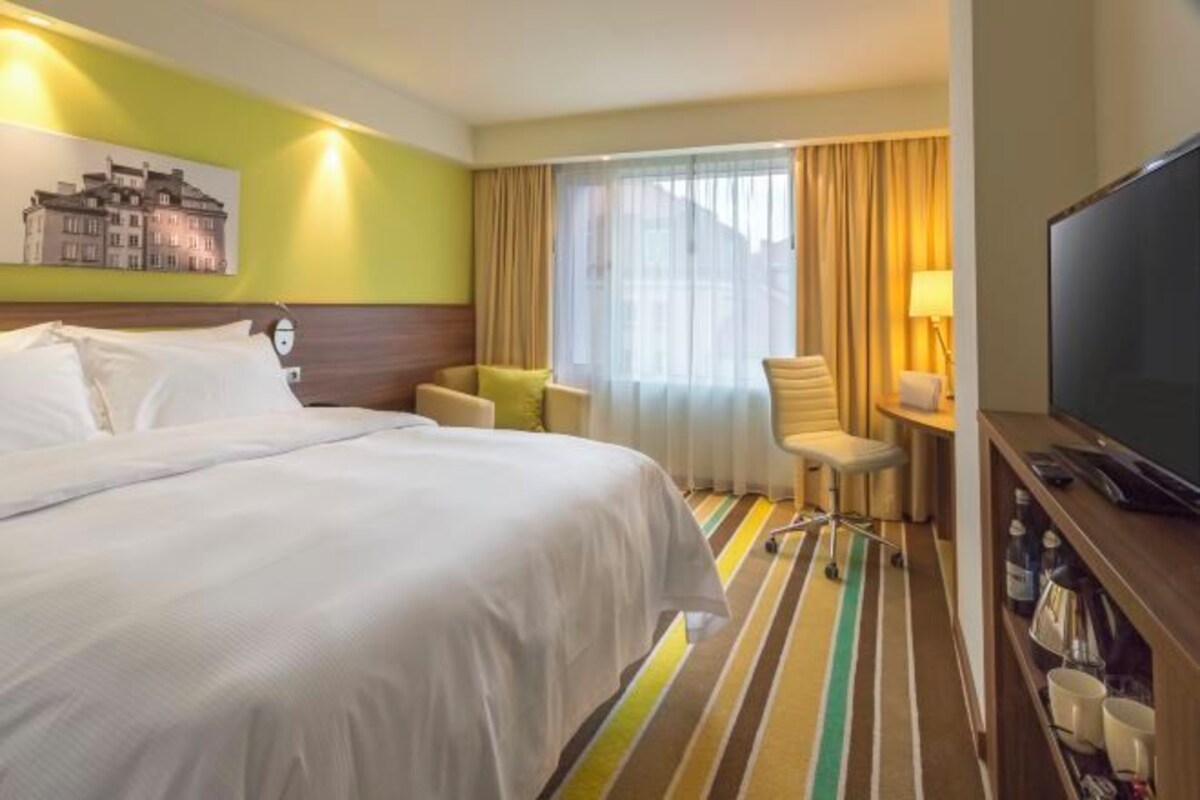 A hotel room with a large bed, a desk with a chair, a television, and a window with curtains.
