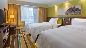 Une chambre d’hôtel avec deux lits, un bureau avec une lampe, une chaise et un téléviseur.