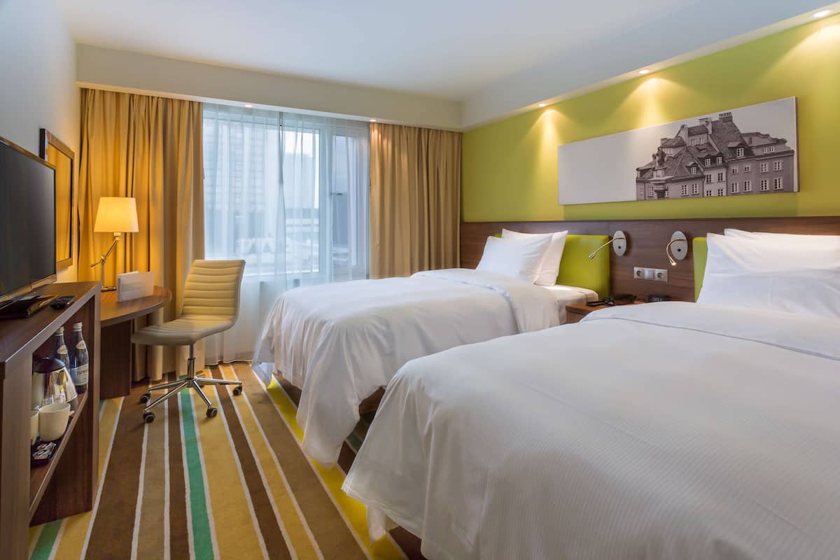 Une chambre d’hôtel avec deux lits, un bureau avec une lampe, une chaise et un téléviseur.