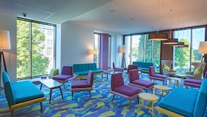 Un hall d'hôtel moderne, doté de meubles colorés, de grandes fenêtres et d'un tapis à motifs.