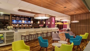 Un espace bar moderne avec un plafond en bois, des chaises colorées et un comptoir bien garni.