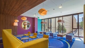 Un hall d'hôtel moderne, doté de sièges aux couleurs vives, de grandes fenêtres et d'un plafond en bois.
