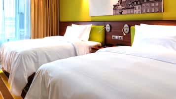 A hotel room with two beds, a large window with curtains, a wall-mounted painting, and a bedside table with a lamp.