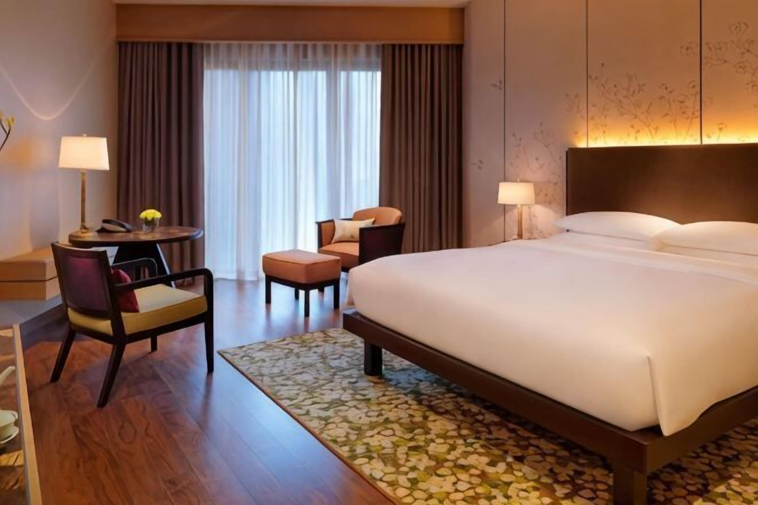 A hotel room with a large bed, a desk with a chair, a small table, and a sofa.