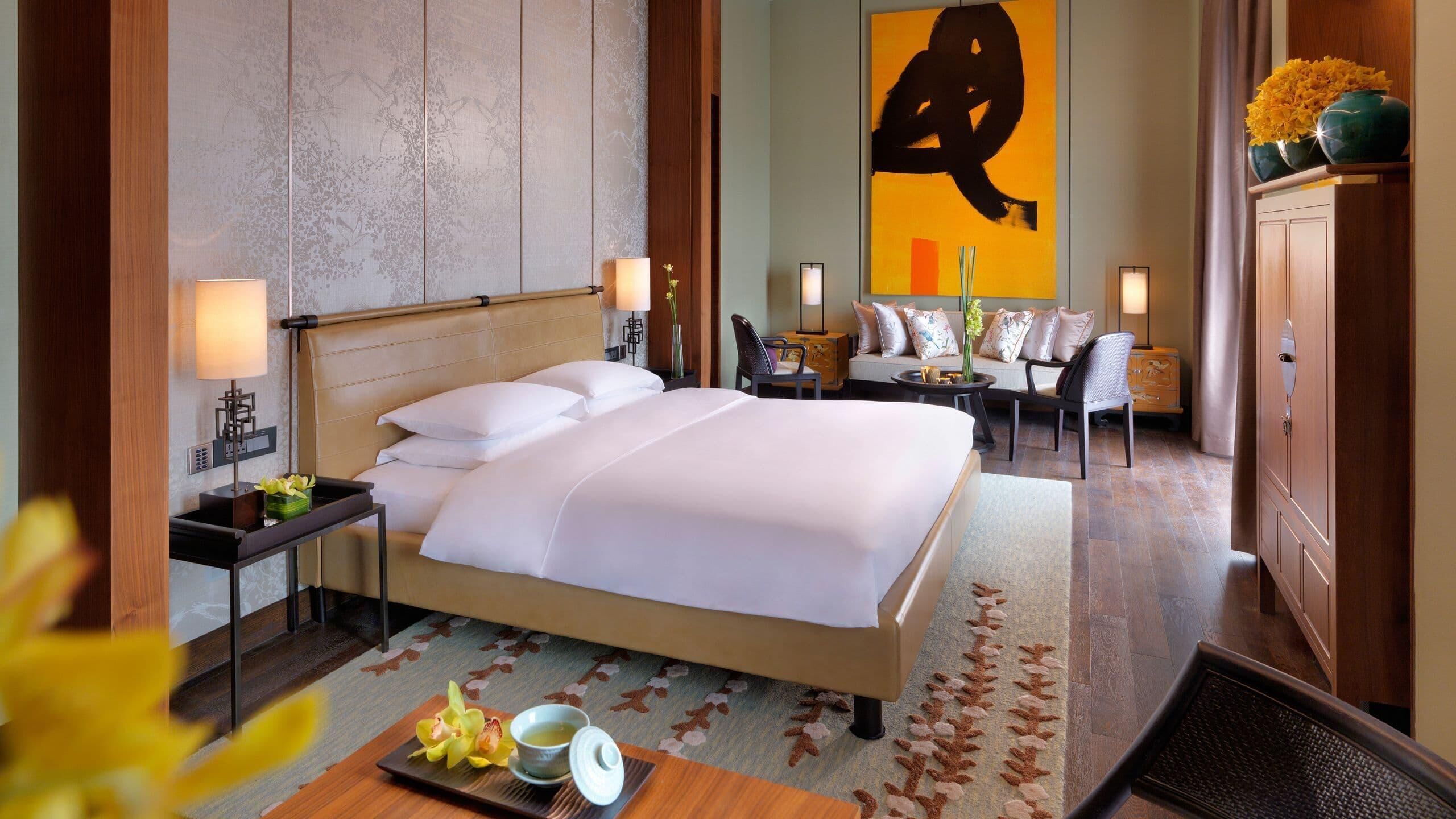 A hotel room with a bed, bedside tables, a sofa, a chair, and a cabinet.