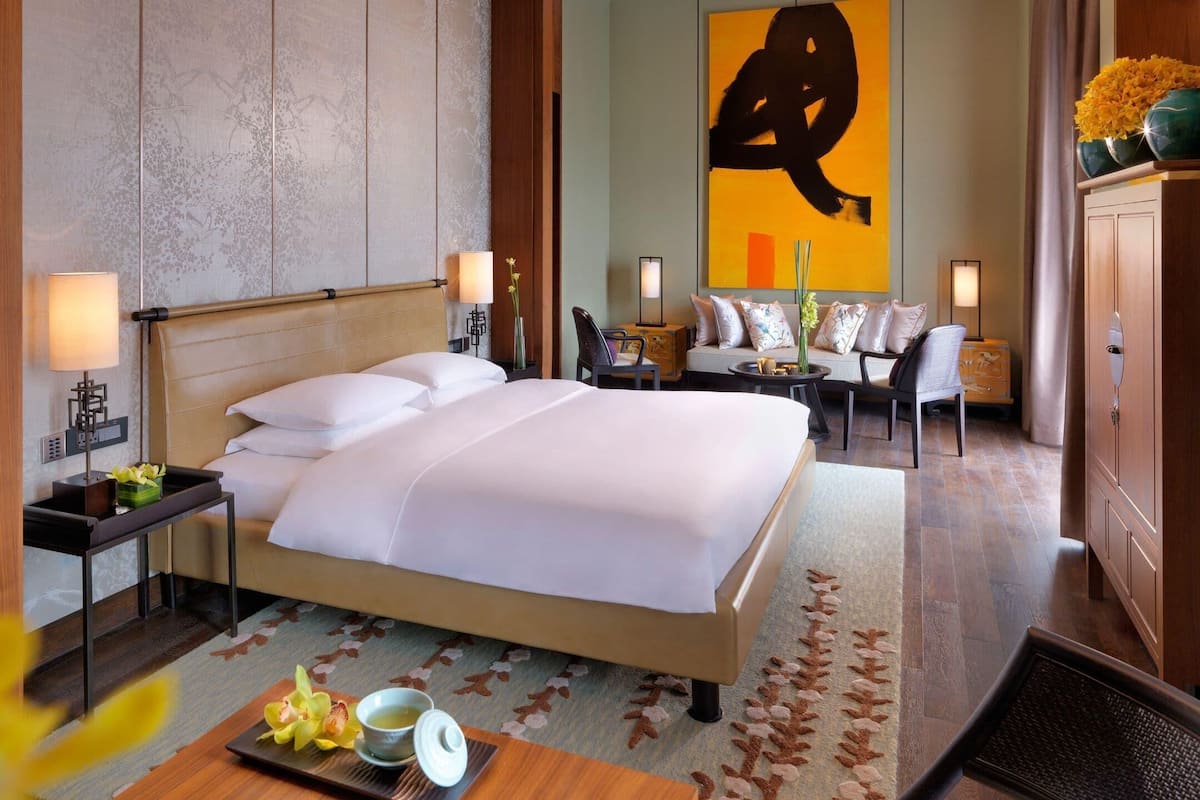A hotel room with a bed, bedside tables, a sofa, a chair, and a cabinet.